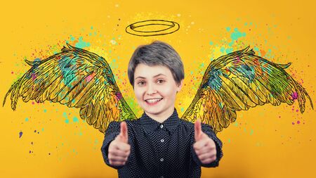 Portrait of happy girl keeps thumbs up over yellow background, smiling broadly imagining herself an...