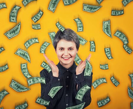 Emotive girl smiles broadly, spreads hands or applause overjoyed, exclaims happiness as money are falling like dollar rain from the sky. Lottery winning, celebrating success. Wealth and good luck.の写真素材