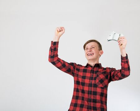 Joyful teenage boy playing video games isolated over white background celebrating success raising...