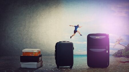 A leap back to summer. Confident young man traveler jumping over his luggage to get back to holiday. Tourist guy needs a vacation in an exotic destination far from workplace.の写真素材