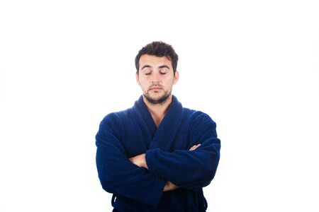 Portrait of sleepy young man wears blue bathrobe with crossed arms eyes closed feel tired needs to sleep isolated on white background.の写真素材