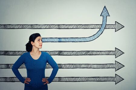 Determined woman, hands on hips, looking up as arrow sketches go straigth ahead and one changing direction bending up. Different thinking concept, break the rules be creative.           People confidence and motivation concept.の写真素材
