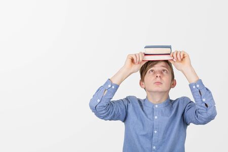 Stressed teenager holding books on his head having exams and feeling overwhelmed, depressed and exhausted . Concept of education.の写真素材