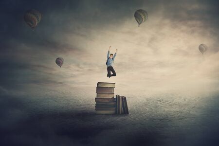 Back to school surreal scene with an overjoyed student boy jumping from the top of a books pile as...
