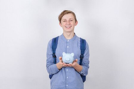 Smiling Teenager boy holding piggy bank over white background. Financial education savings concept.の写真素材