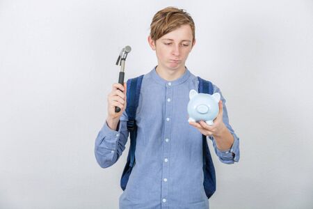Frustrated student boy try to break a piggy bank using a hammer isolated over white background. Small amount of financial savings, not enough money for study contract.の写真素材