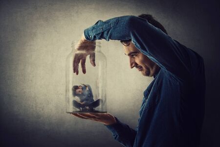 Conceptual scene, scared tiny boy trapped inside a glass jar held in hand by a scary giant. Surreal nightmare, child adoption through the eyes of a teen. Helpless captive kid victim of family abuse.の写真素材