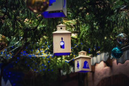 Blue light lantern like Christmas decorations and globes hanging on green fir tree branches above...