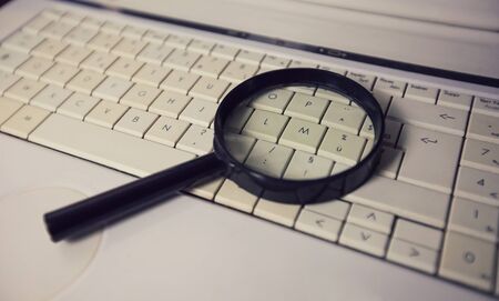 Close up of a magnifying glass on an old laptop keyboard. Computer search engine. Browsing network...
