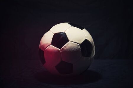 A red spot of light casting on the classic soccer ball isolated on a black background. Dark mood as all the championships and tournaments are closing due to Coronavirus pandemic outbreak.の写真素材