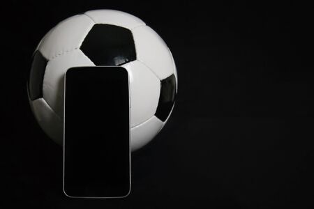 Live football betting concept, blank smartphone screen and classic football ball isolated on black background with copy space. Sports gambling app, entertainment games, play soccer on mobile phone.の写真素材
