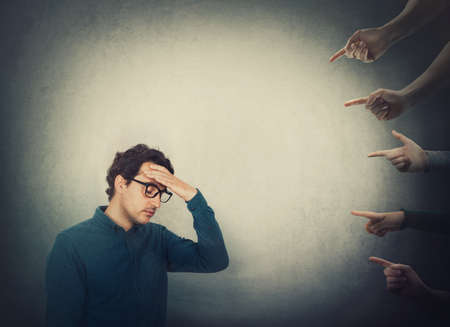 Exhausted businessman suffers dizziness, feels discomfort as multiple people hands pointing to him blaming as guilty. High tension and pressure, depression and emotional stress. Social victim concept.の写真素材