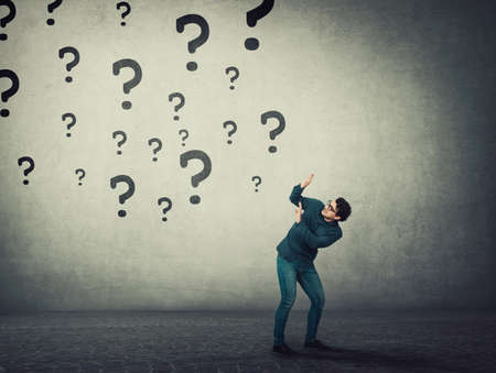 Scared man keeps hands raised up to protect him from multiple questions threat falling above him as...