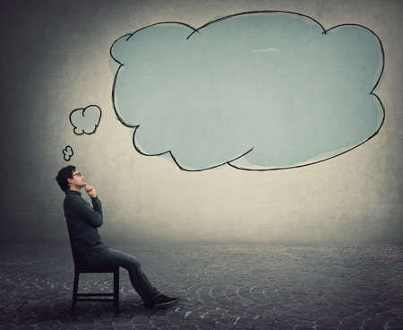 Side view businessman sitting on chair, keeps hand under chin, thoughtful gesture, and an empty thought bubble, thinking cloud, comes out of his head. Business employee focused on ideas and planning.の写真素材