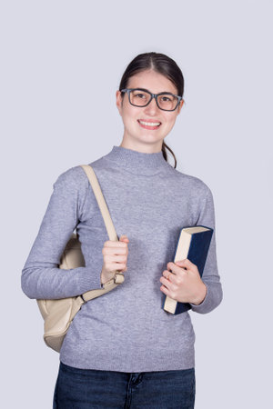 Confident student girl smiling holding one books and carrying her backpack. Cheerful student girl with positive face expression isolated on white background.の写真素材