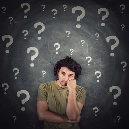 Melancholic young man, long curly hair style, keeps one fist under cheek, looks doubtful and unsure...