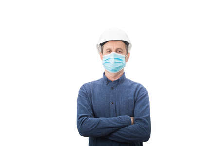 Serious confident middle aged architect wearing protective helmet and face mask protection against the Covid-19 or coronavirus arms crossed looking to camera isolated over white background ..の写真素材
