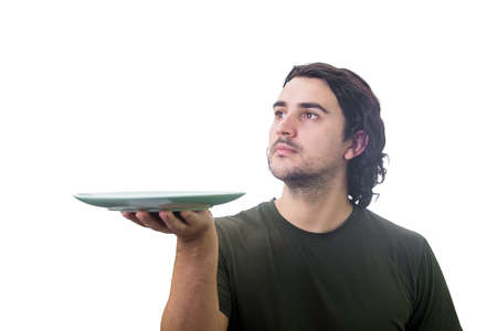 Young man waiter holding an empty dish plate in his hands isolated on white background. People has no food to eat after drought season. Global crisis and hunger issue. Famine and starvation conceptの写真素材