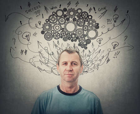 Confident middle aged man, brainstorming concept, has a cogwheel brain above head. Senior male mental health, positive thinking and psychological development symbolの写真素材