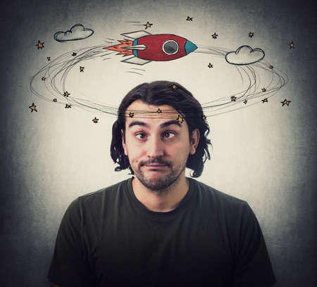 Silly young man makes funny dumb faces with crossed eyes. Body language emotional reaction. Dizzy daydreaming, stars and rocket making circles around his head. Guy suffering from strabismusの写真素材