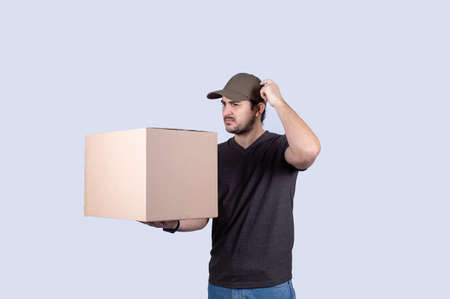 Pensive delivery man hand to head with thoughtful gesture, holding a box isolated on white background. Courier man holding box having problem with delivery over white background.の写真素材
