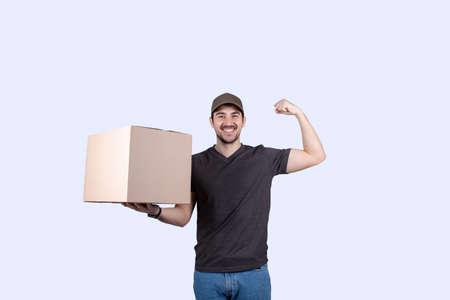 Happy delivery man holding a box package and felxing one hand biceps imagine superpower. Confident courier worker. Personal development, power and motivation concept.の写真素材