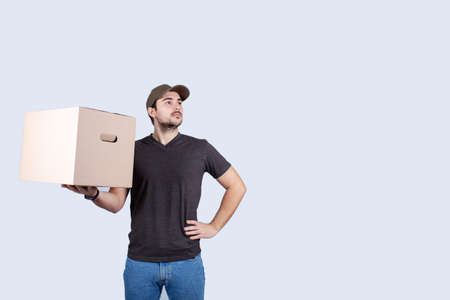 Delivery man holding a box package hands on hips showing chest, brave gesture keeps arms crossed confident, casting a superhero. Worker Ambition and business success concept. Leadership hero power, motivation and inner strength symbol.の写真素材