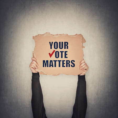 Activist hands holding up a cardboard banner with text message your vote matters, isolated on gray...