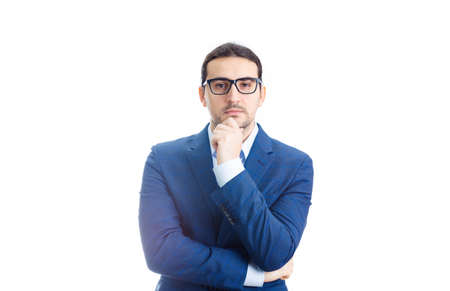 Young businessman keeps hand under chin, Thoughtful gesture, isolated over white background. Business worker wears glasses looking to camera, thinking of great ideas.の写真素材