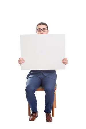 Businessman seated on chair holding a big blank banner with copy space for messages. Full length business person with empty advertising placard. Warning and advertisement conceptの写真素材