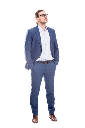 Full length portrait of confident businessman keeps hands in his pockets looking thoughtful isolated on white background. Business person thinking for solutionsの写真素材