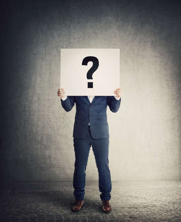 Anonymous businessman covering head using a banner with interrogation mark, like a mask to hide emotions and identity. Full length unknown person with hidden face behind question symbolの写真素材