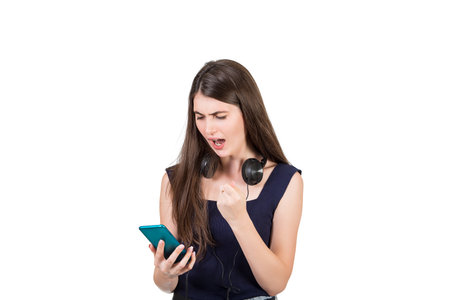 Bewildered young woman with headphones looking shocked, mouth open at her smartphone, isolated on white background.の写真素材