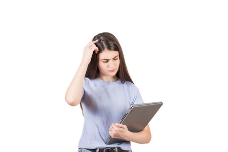 Puzzled young woman holding a defect laptop in her hand, looking thoughtful at it, scratching her head, isolated on white backgroundの写真素材