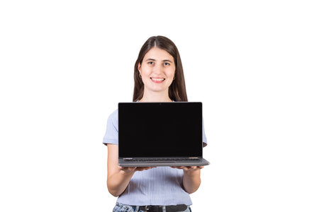Cheerful young woman holding a laptop in her hands showing the blank screen to camera isolated on white background. PC recommendation, marketing and advertising conceptの写真素材