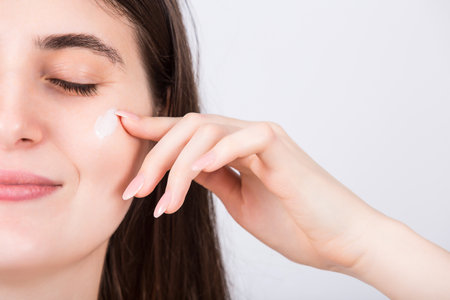 Closeup woman face applying moisturizing cream, isolated on white background. Skin care conceptの写真素材