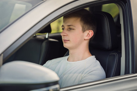 Young man driving safe his new car, looking focused ahead at the street traffic. Confident teenage driver enjoying the ride, traveling road trip conceptの写真素材