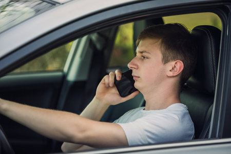 Young man unsafe driving while phone talking in front of the steering wheel. Careless driver violates traffic rulesの写真素材