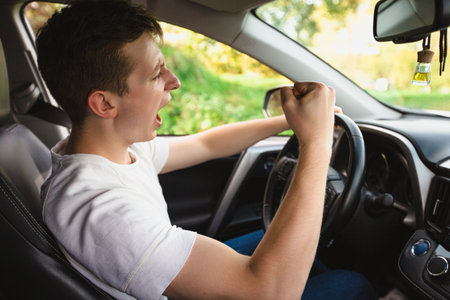 Novice driver screaming sitting in his car behind the wheel shaking his fist threatens another motorist. Bad and aggressive behavior on road concept.の写真素材