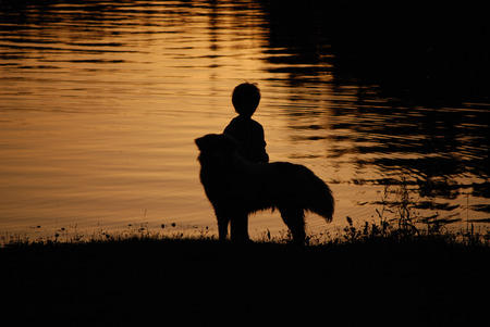 A boy and his dog enjoy the sunset on the beach of a mountain lake.の写真素材