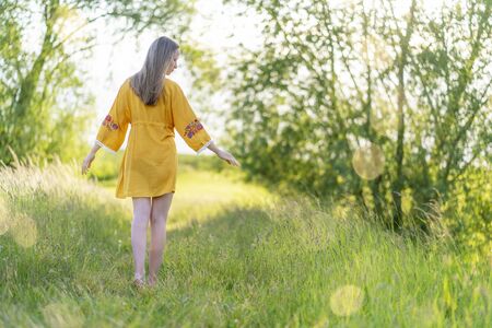 Young girl posing in nature in yellow summer dress in the light-flooded evening lightの写真素材