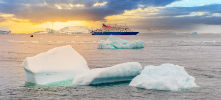 blue expedition ship in front of antarctic iceberg landscape in Cierva Cove - a deep inlet on the west side of the Antarctic Peninsula, surrounded by dramatic glacier frontsの写真素材