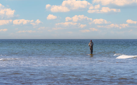 An angler in waterproof trousers is fishing in the Baltic Sea. He is standing on a stone in the water - Sunset on the Baltic Sea with a lone fisherman in the waterの写真素材