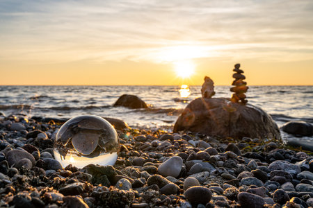 Sunset on the beach with a stack of stones in the foreground - Stone pyramids and glass sphere on the dreamy Baltic Sea sand beach on RÃ¼gen for the spectacular sunsetの写真素材