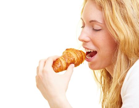 Happy woman eating a croissant at breakfastの写真素材