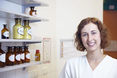 Happy female pharmacy technician in lab with shelfの写真素材