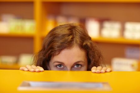 Female pharmacist looking up behind counter in pharmacyの写真素材