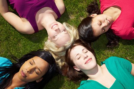 Four young women sunbathing in a park with eyes closedの写真素材
