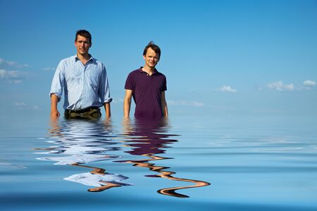 Two young men walking through blue water
