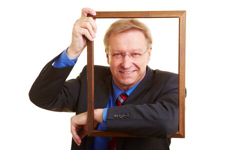 Smiling senior businessman leaning in an empty picture frameの写真素材